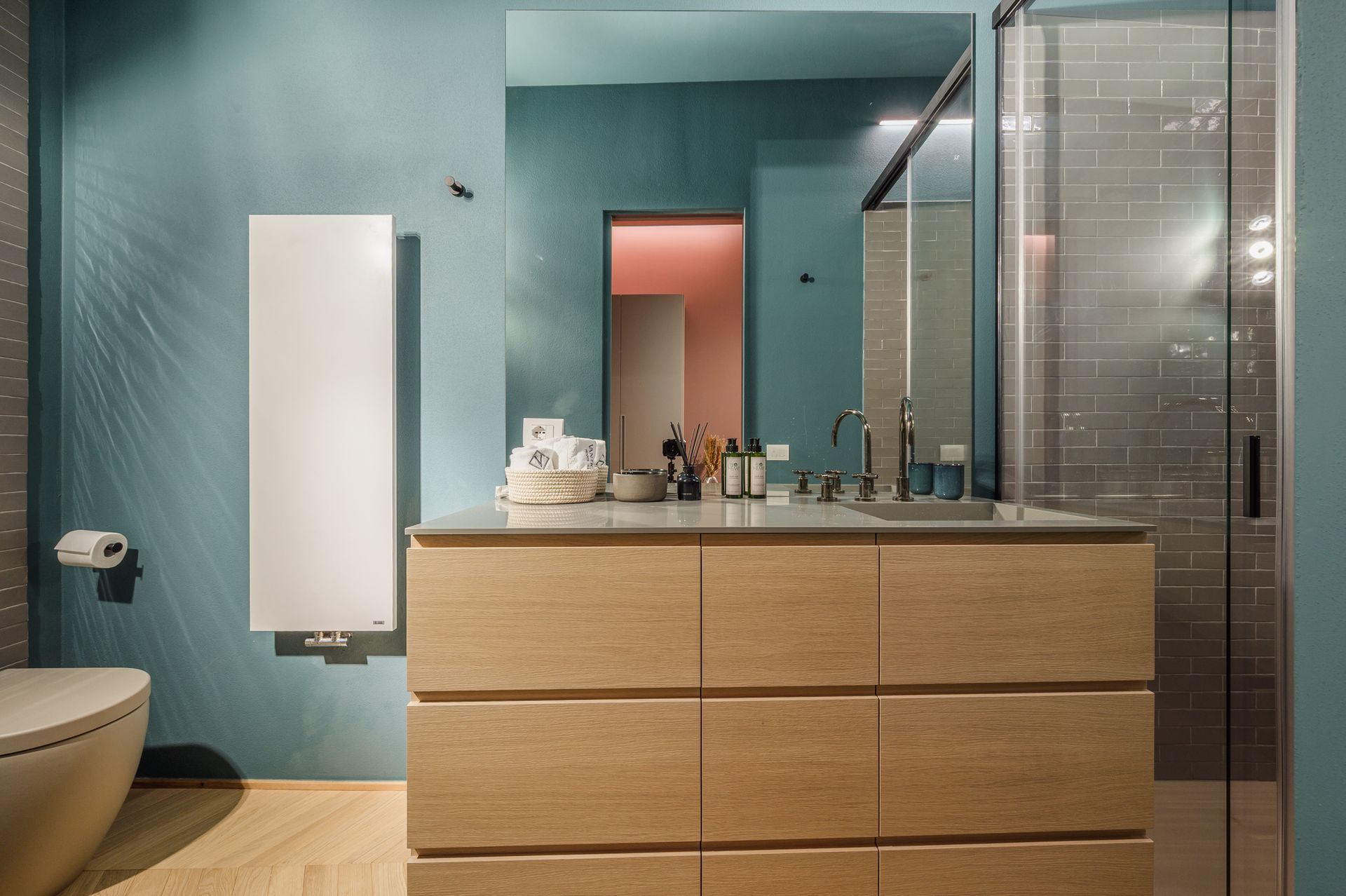 Vanity del bagno turchese con specchio che riflette il bagno rosa sullo sfondo