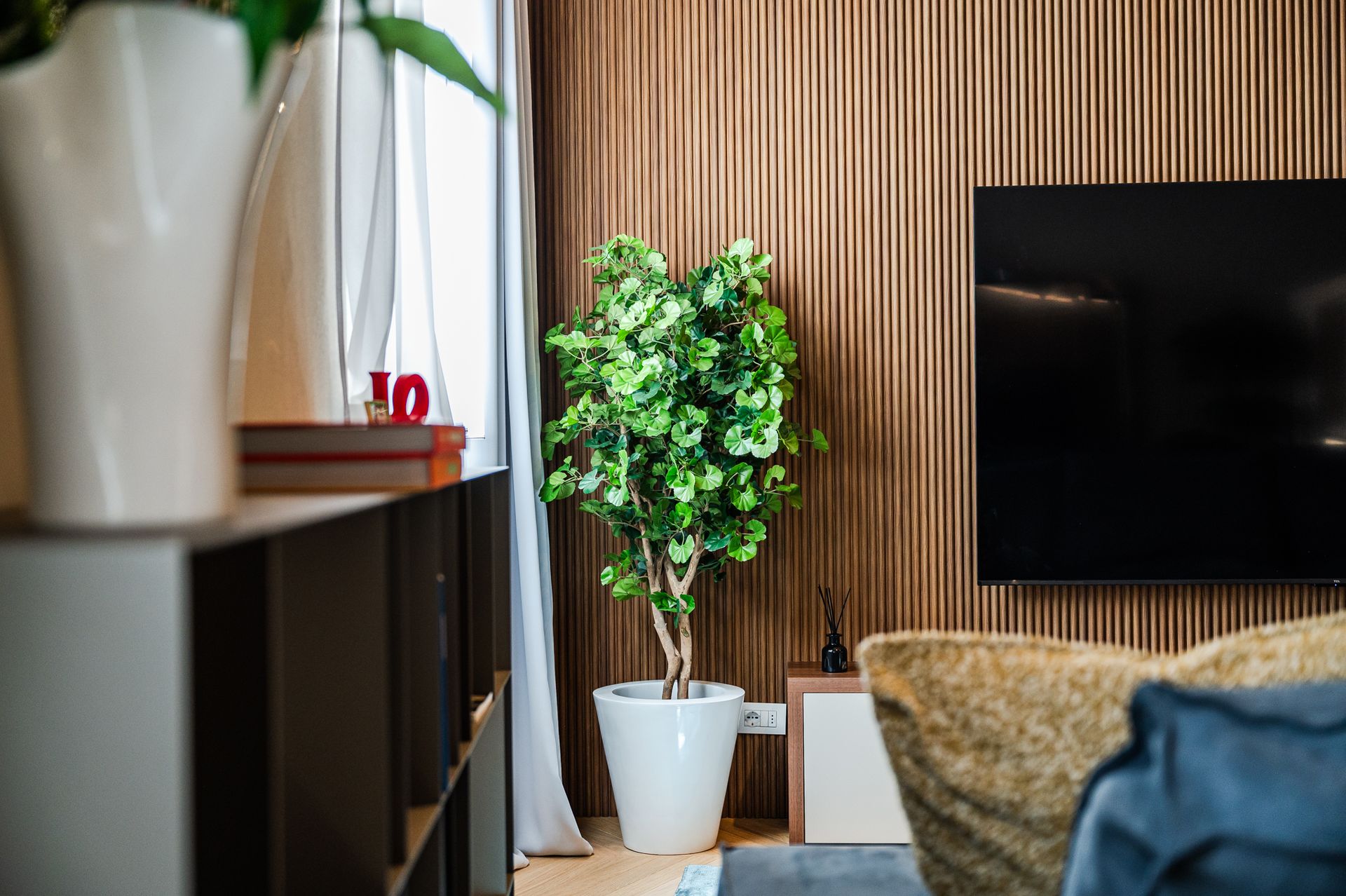 Angolo del living con pianta, TV a parete e divano blu-grigio